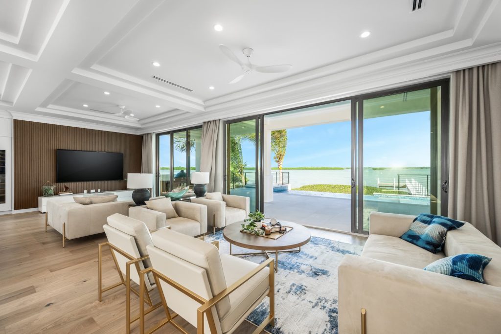 Luxury waterfront living room featuring expansive sliding glass doors, modern seating, wood flooring, and an open terrace with panoramic water views
